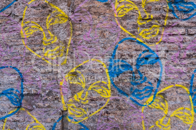 Worn brick wall with graffiti faces background texture.