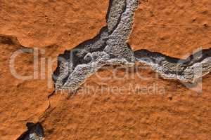 Orange peeling paint on a grey cracked concrete wall.