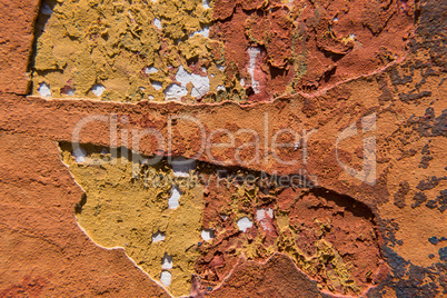 Cracked orange paint on a yellow concrete wall.