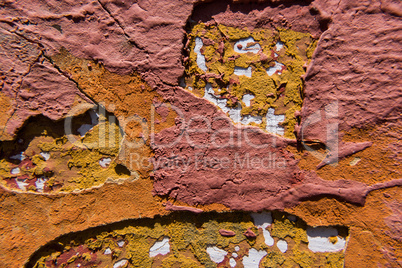 Cracked orange and red paint on a yellow concrete wall.