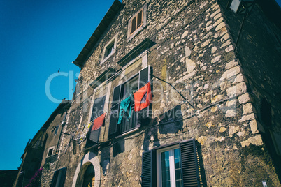 Red and green clothes hanged in front of a stone medieval house.
