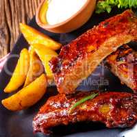 bbq spareribs on the plate with green salad and white sauce.