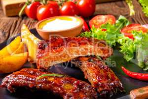 bbq spareribs on the plate with green salad and white sauce.