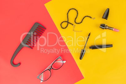 Glasses, cosmetics, jewelry and comb on a yellow and red backgro