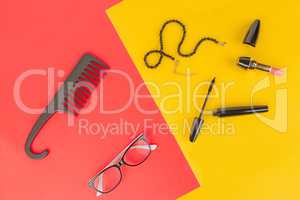 Glasses, cosmetics, jewelry and comb on a yellow and red backgro