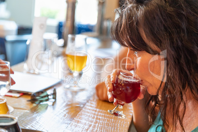 Female Sipping Glass of Micro Brew Beer At Bar With Friends