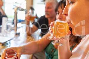 Female Sipping Glass of Micro Brew Beer At Bar With Friends