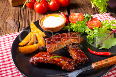 bbq spareribs on the plate with green salad and white sauce.