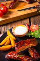 bbq spareribs on the plate with green salad and white sauce.