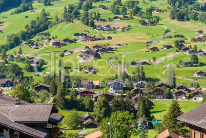 The picturesque Swiss town of Grindelwald. Traditional wooden chalets in summer, in front of the North side of the Eiger mountain, surrounded by bright green pastures