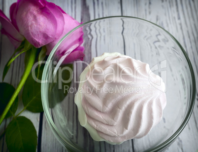 A marshmallow in a glass vase next to a rose.