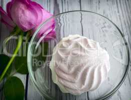 A marshmallow in a glass vase next to a rose.