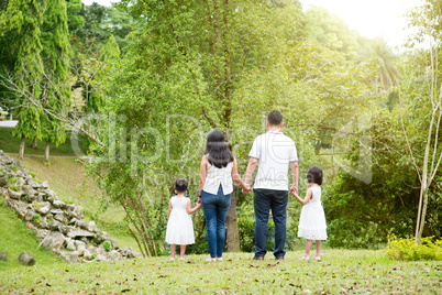 Asian family hold hands walking at outdoor park, back view.