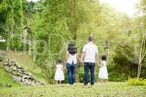 Asian family hold hands walking at outdoor park, back view.