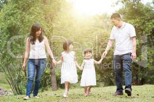 Asian family hold hands walking at outdoor park.