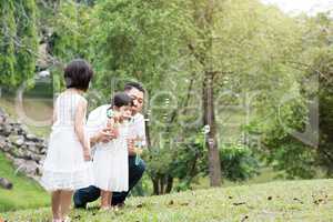 Happy Asian family blowing soap bubbles at park