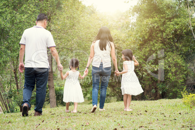 Asian family hold hands and walking at outdoor park, back view.