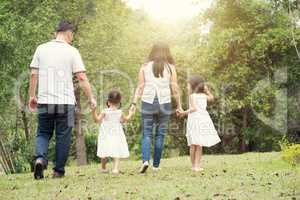 Asian family hold hands and walking at outdoor park, back view.