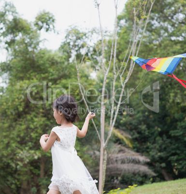 Little girl flying kite at park.