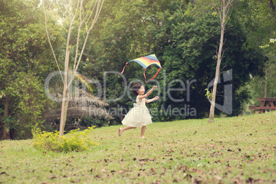 Happy little Asian girl flying kite at park.