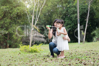 Mother and daughter blowing soap bubbles outdoors