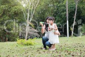 Mother and daughter blowing soap bubbles outdoors