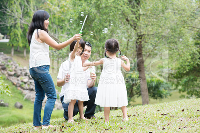 Asian family blowing soap bubbles at park