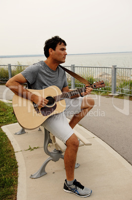 Young man playing the guitar on a bench
