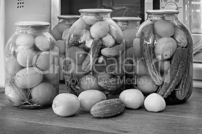 Canned tomatoes and cucumbers in large glass jars. Black-and-white image.