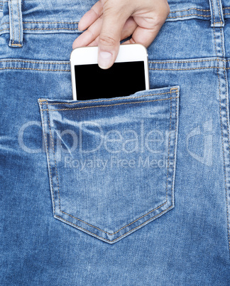 female hand holds a white phone in the back of the blue jeans