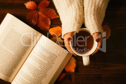 Woman hands holding teacup and opened book seen from above