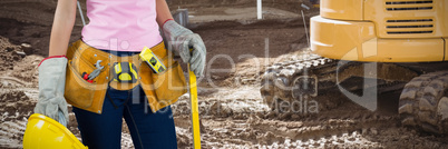 Composite image of woman with tool belt and holding hard hat against grey background