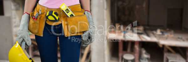 Composite image of woman with tool belt and holding hard hat against grey background