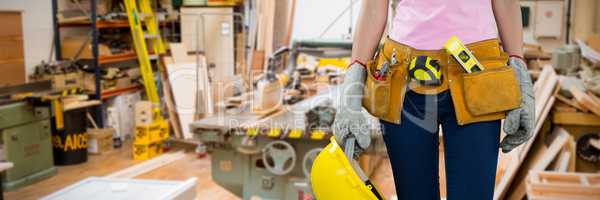 Composite image of woman with tool belt and holding hard hat against grey background