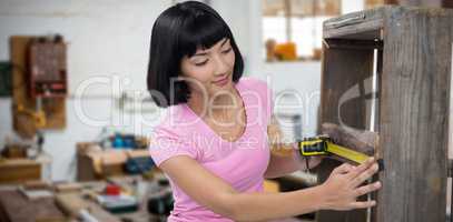 Composite image of woman measuring furniture with tape measure