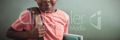 Portrait of boy with backpack and books against greenboard