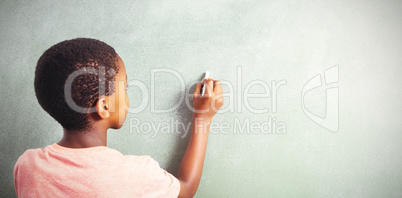 Boy writing with chalk on greenboard in school