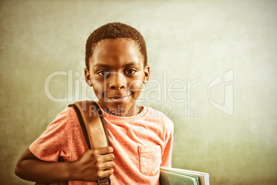 Portrait of boy with backpack and books against greenboard