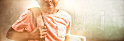 Portrait of boy with backpack and books against greenboard