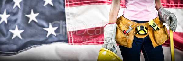 Composite image of woman with tool belt and holding hard hat against grey background