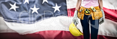 Composite image of woman with tool belt and holding hard hat against grey background