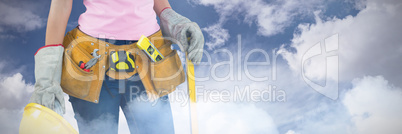 Composite image of woman with tool belt and holding hard hat against grey background