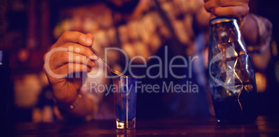 Waiter pouring cocktail drink into shot glasses at counter