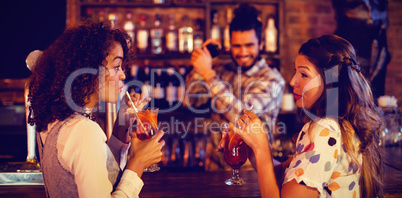 Two young women having cocktail drinks at counter