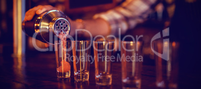 Waiter pouring cocktail drink into shot glasses at counter