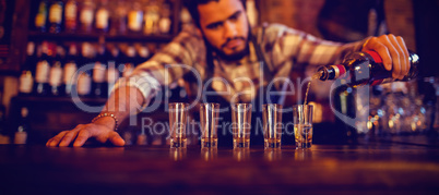 Waiter pouring tequila into shot glasses at counter