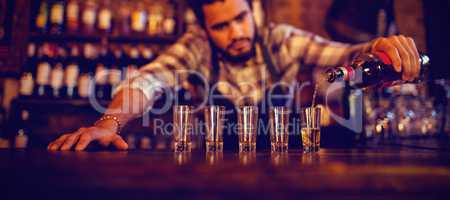 Waiter pouring tequila into shot glasses at counter