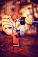 Waiter pouring cocktail drink into shot glasses at counter