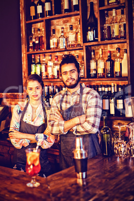 Portrait of waiter and waitress standing with arms crossed at counter