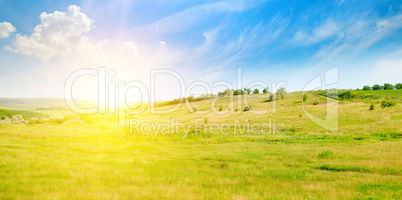 Hilly green fields and sunrise on a blue sky. Wide photo.